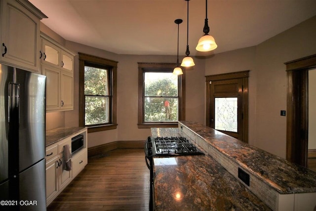 kitchen featuring black refrigerator, decorative light fixtures, white cabinetry, and dark stone counters