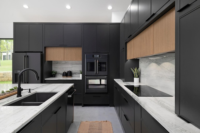 kitchen with light stone countertops, a sink, dark cabinetry, decorative backsplash, and black appliances