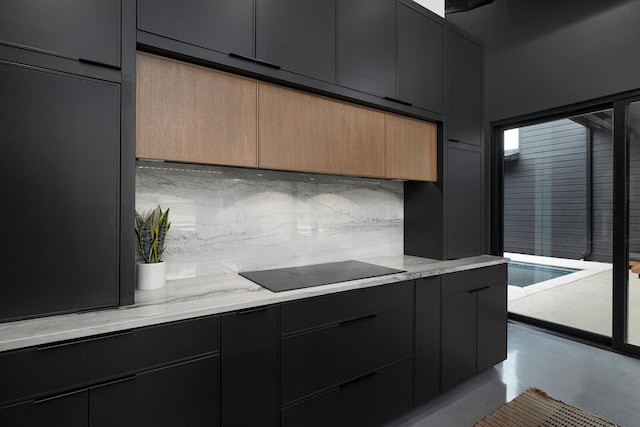 kitchen with dark cabinetry, concrete floors, backsplash, and black electric cooktop