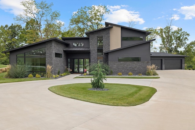 view of front facade with driveway, stone siding, an attached garage, a standing seam roof, and a front yard