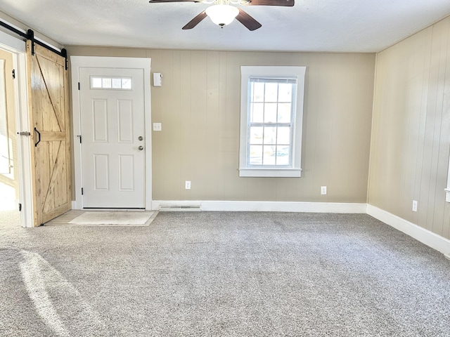 carpeted foyer entrance with wood walls, ceiling fan, and a barn door