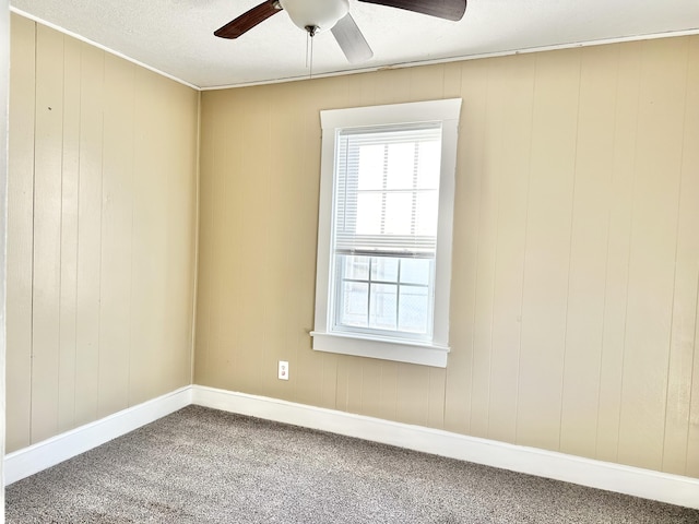 empty room with ceiling fan, wooden walls, and carpet