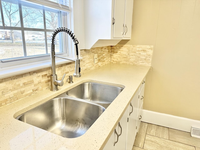 kitchen with light stone counters, white cabinets, backsplash, and sink