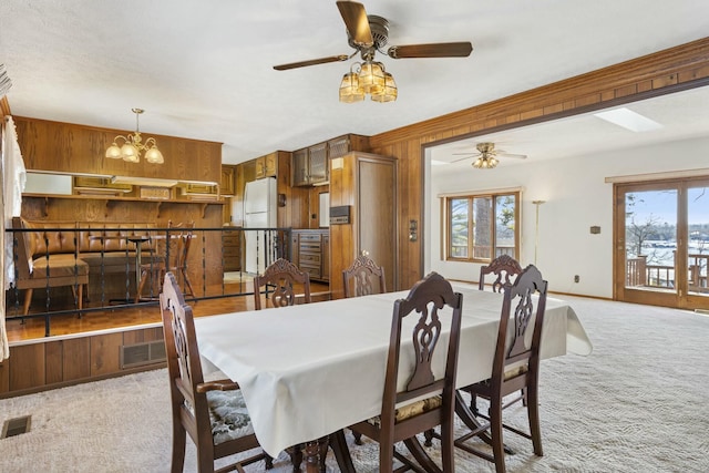 dining area featuring light colored carpet, wooden walls, and ceiling fan with notable chandelier