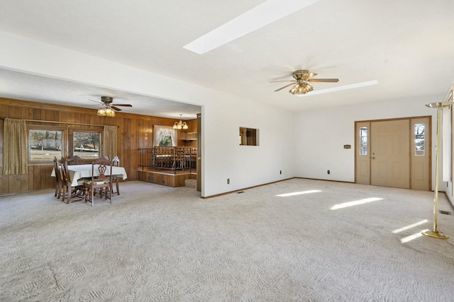 unfurnished living room featuring a skylight, light carpet, wood walls, and ceiling fan with notable chandelier