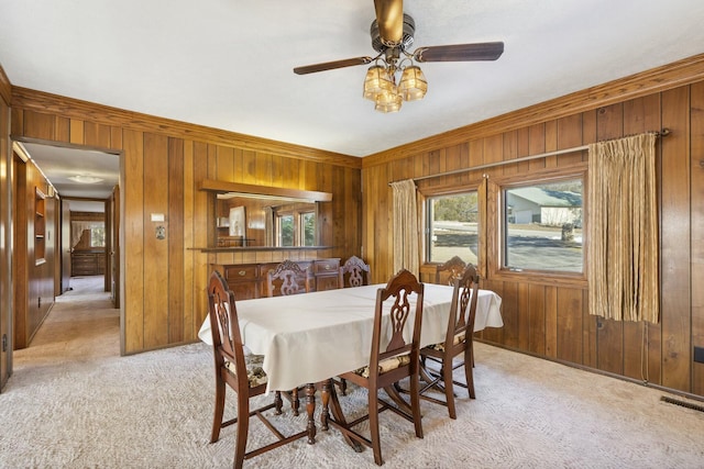 carpeted dining space featuring wood walls, ceiling fan, and crown molding