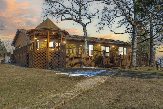 back house at dusk featuring cooling unit, a yard, and a wooden deck