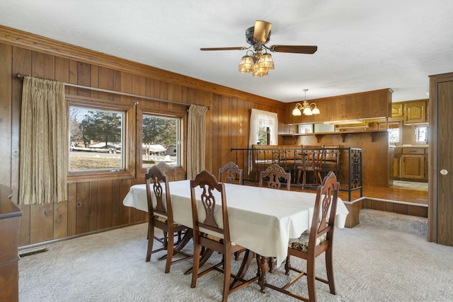 carpeted dining room featuring ceiling fan with notable chandelier and wood walls