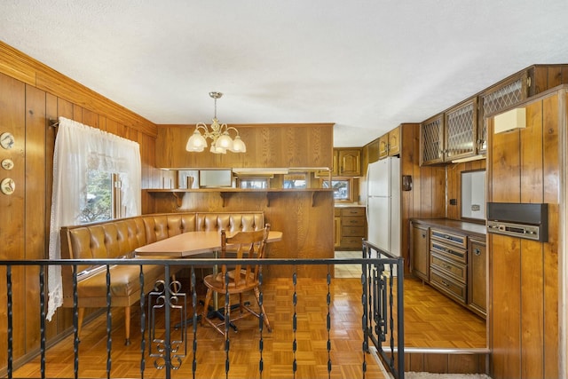 kitchen with a notable chandelier, white refrigerator, wood walls, and parquet floors