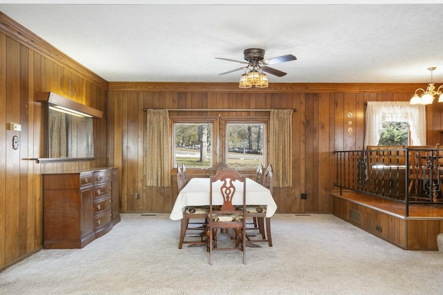 dining space featuring ceiling fan with notable chandelier, light colored carpet, wooden walls, and crown molding