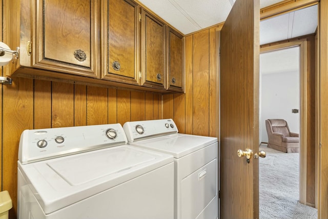 clothes washing area featuring light colored carpet, washing machine and dryer, wooden walls, and cabinets