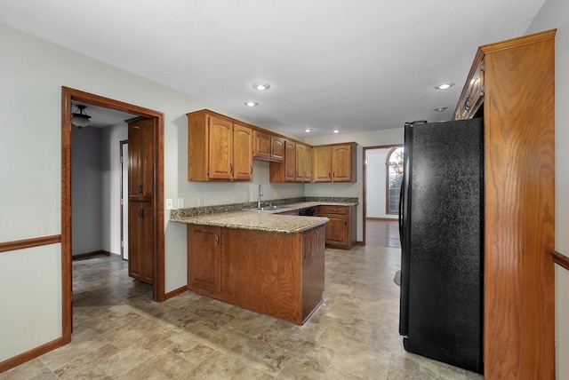 kitchen featuring black fridge, sink, kitchen peninsula, and light stone countertops