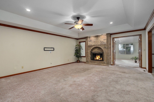 unfurnished living room with ceiling fan, a fireplace, a tray ceiling, ornamental molding, and light carpet