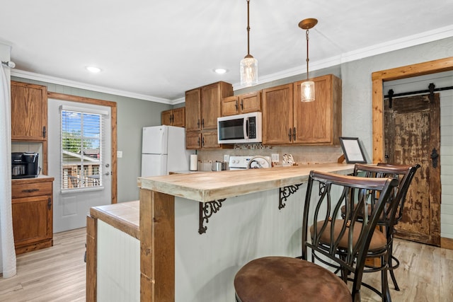 kitchen with pendant lighting, white appliances, a barn door, light wood-type flooring, and a breakfast bar area