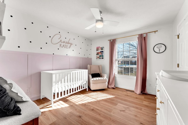 bedroom featuring light hardwood / wood-style floors, a nursery area, and ceiling fan