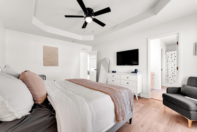 bedroom with ceiling fan, ensuite bathroom, light hardwood / wood-style flooring, and a raised ceiling