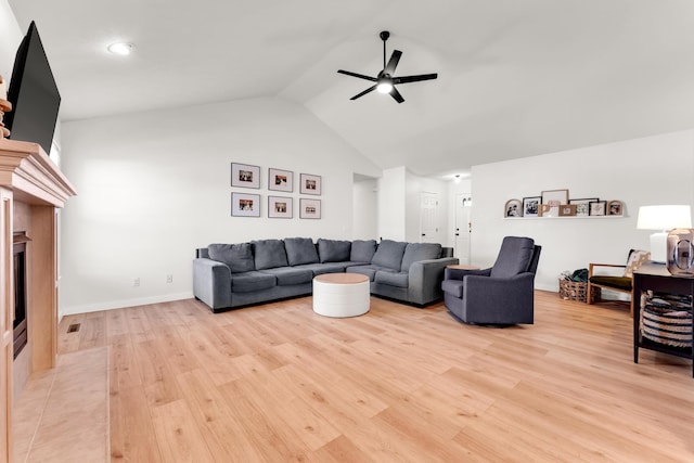 living room featuring ceiling fan, light wood-type flooring, a fireplace, and vaulted ceiling