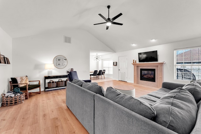 living room with ceiling fan with notable chandelier, light hardwood / wood-style flooring, lofted ceiling, and a tiled fireplace