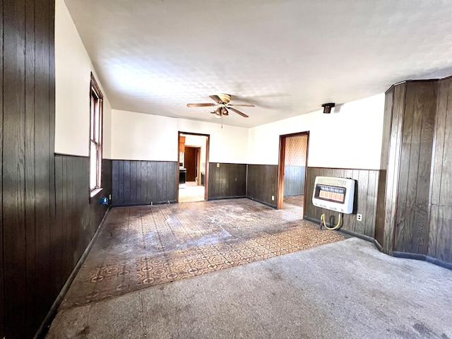 unfurnished living room featuring a textured ceiling, wood walls, ceiling fan, and heating unit