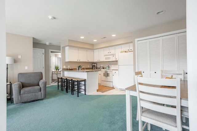 kitchen with white appliances, a kitchen breakfast bar, light carpet, an island with sink, and white cabinets