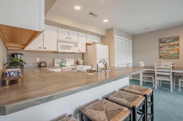 kitchen featuring white appliances, kitchen peninsula, a breakfast bar, carpet flooring, and white cabinetry