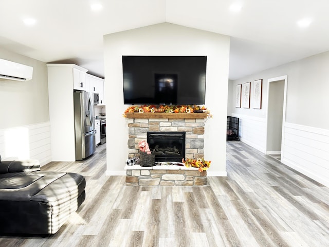 living room with lofted ceiling, a fireplace, a wall mounted AC, and light hardwood / wood-style flooring