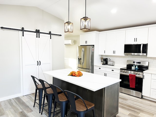 kitchen featuring stainless steel appliances, decorative light fixtures, lofted ceiling, a barn door, and a breakfast bar