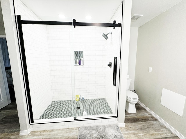 bathroom featuring toilet, wood-type flooring, and a shower with door