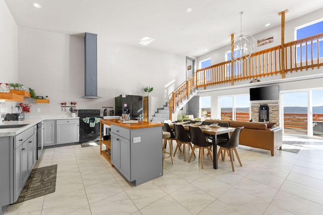 kitchen featuring wall chimney range hood, black appliances, butcher block counters, and gray cabinetry