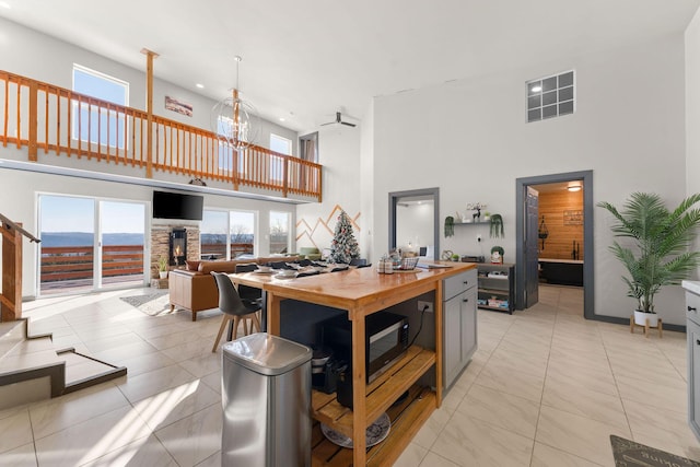 kitchen featuring a towering ceiling, a breakfast bar area, light tile patterned floors, butcher block counters, and ceiling fan with notable chandelier