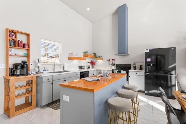 kitchen with a center island, black appliances, sink, a kitchen breakfast bar, and wall chimney exhaust hood