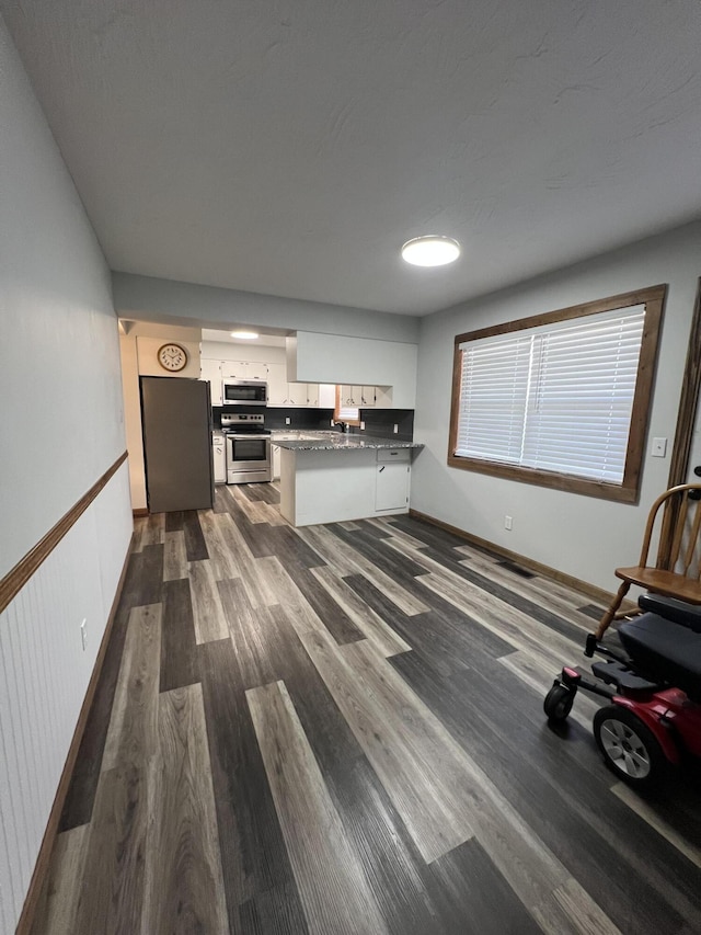 kitchen featuring kitchen peninsula, appliances with stainless steel finishes, white cabinets, and dark wood-type flooring