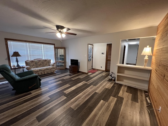 living room featuring ceiling fan, dark wood-type flooring, and a textured ceiling