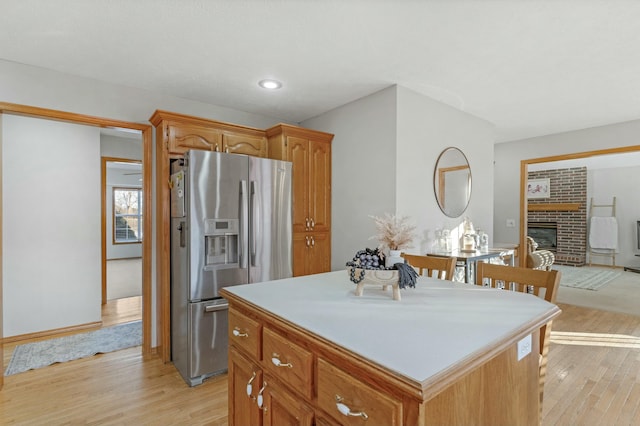 kitchen with light wood-type flooring, stainless steel refrigerator with ice dispenser, a fireplace, and a center island