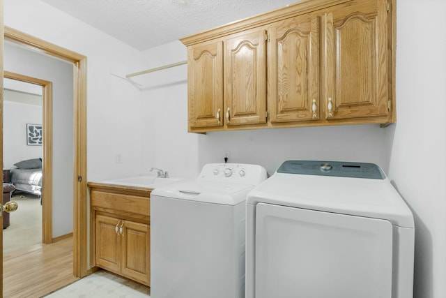 clothes washing area with a textured ceiling, cabinets, washing machine and clothes dryer, sink, and light hardwood / wood-style flooring