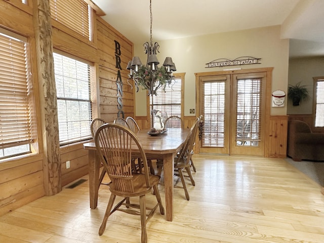 dining area featuring light hardwood / wood-style flooring, a healthy amount of sunlight, a chandelier, and wooden walls