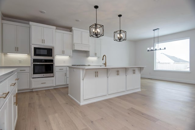 kitchen featuring backsplash, decorative light fixtures, a kitchen island with sink, built in microwave, and oven