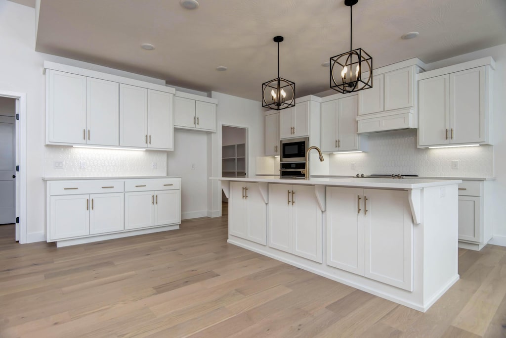 kitchen with built in microwave, white cabinetry, and an island with sink