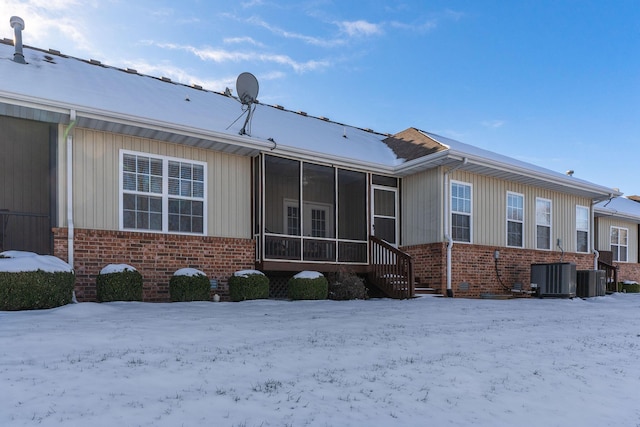 view of snowy exterior featuring central AC unit and a sunroom