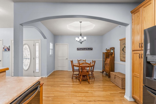 dining space featuring a notable chandelier, a tray ceiling, and light hardwood / wood-style floors