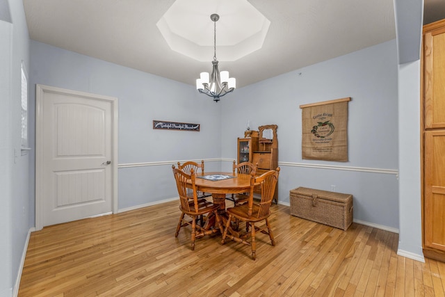 dining space with a notable chandelier, a tray ceiling, and light hardwood / wood-style flooring