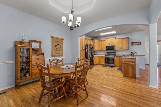 dining room featuring sink, a raised ceiling, a chandelier, and light wood-type flooring