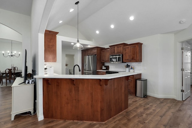 kitchen with lofted ceiling, pendant lighting, kitchen peninsula, an inviting chandelier, and appliances with stainless steel finishes