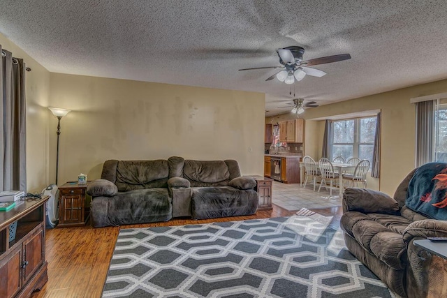 living room featuring ceiling fan, light wood-type flooring, and a textured ceiling