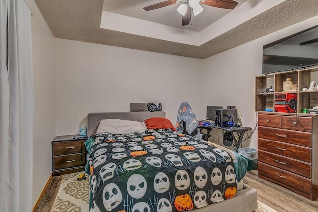 bedroom with ceiling fan, light hardwood / wood-style floors, and a tray ceiling