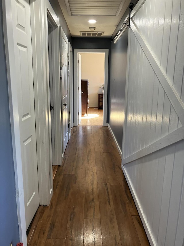 hallway with dark wood-type flooring and a barn door