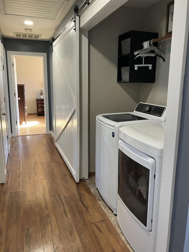 laundry area with washer and clothes dryer, a barn door, and hardwood / wood-style flooring