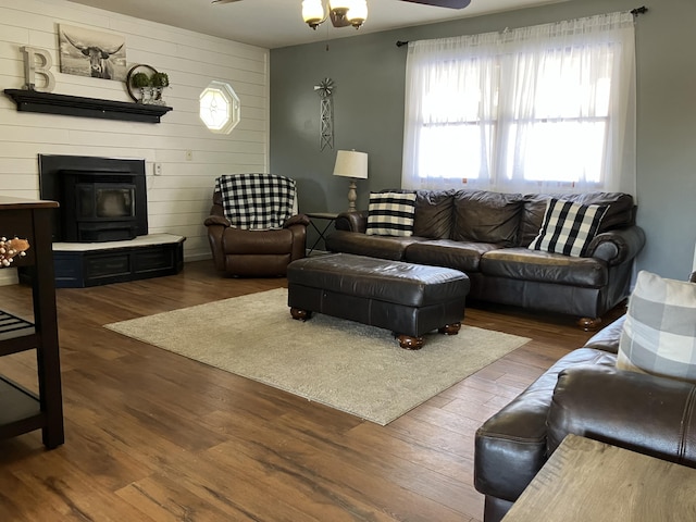 living room featuring ceiling fan, a wood stove, dark hardwood / wood-style flooring, and wooden walls