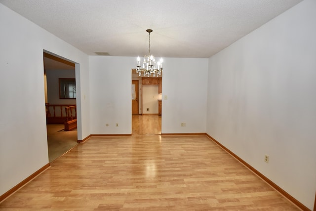 unfurnished room with visible vents, a textured ceiling, light wood-style flooring, and a notable chandelier