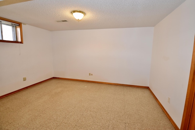 empty room featuring a textured ceiling, light floors, visible vents, and baseboards